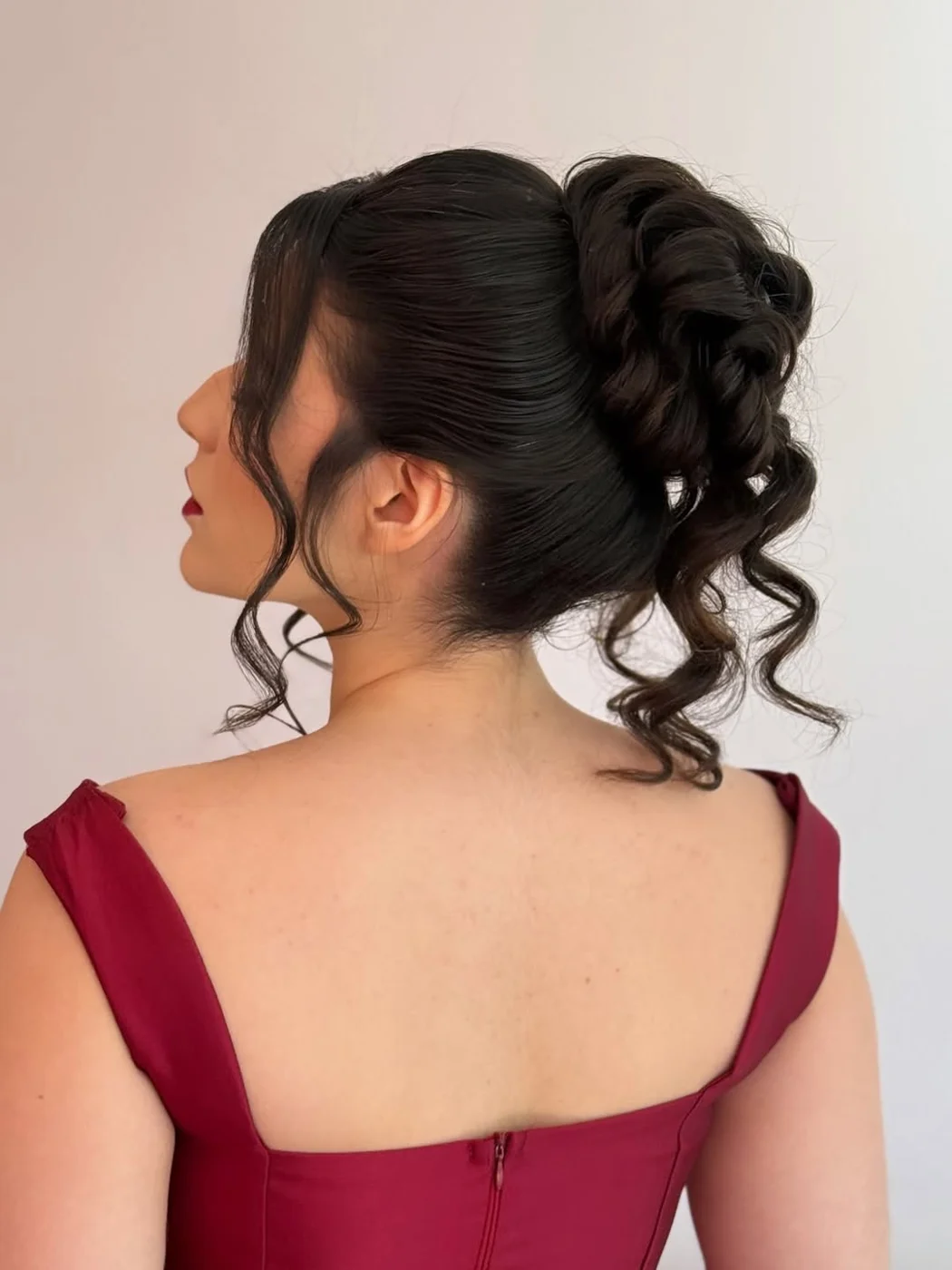 Rabo alto volumoso em cachos, com franja, cliente de vestido vinho vista de perfil