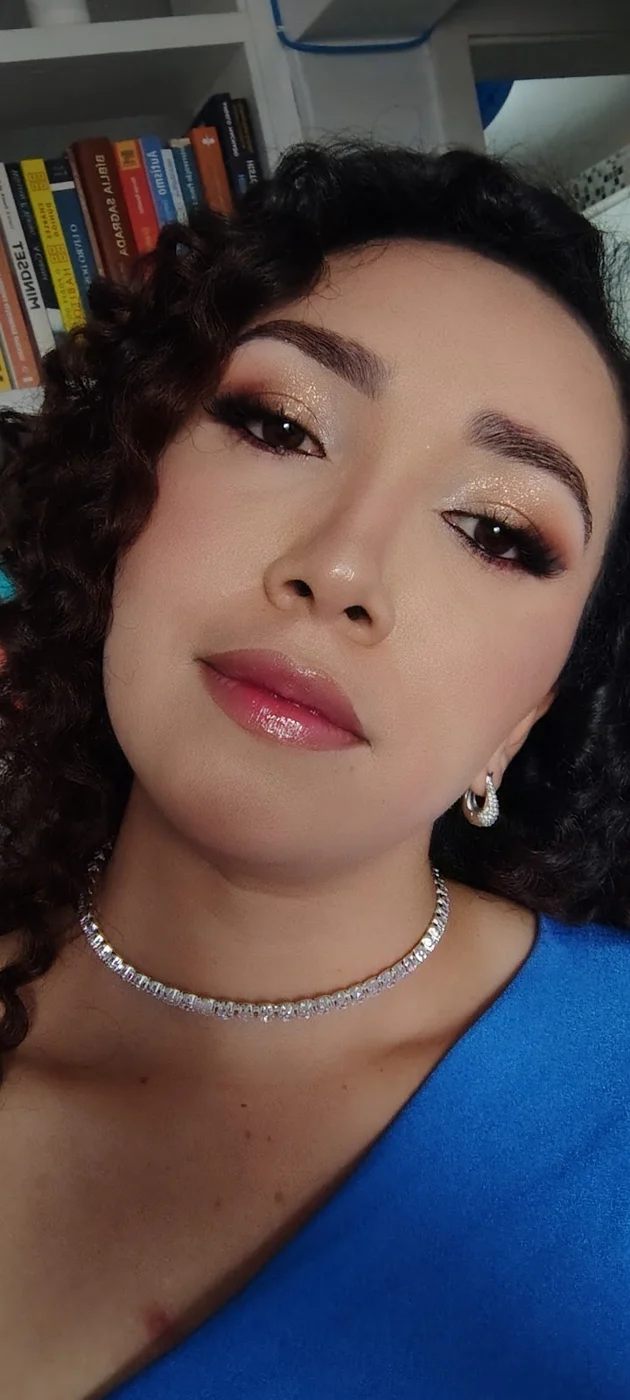 Formanda de cachos e vestido azul, com maquiagem iluminada e colar de brilhantes