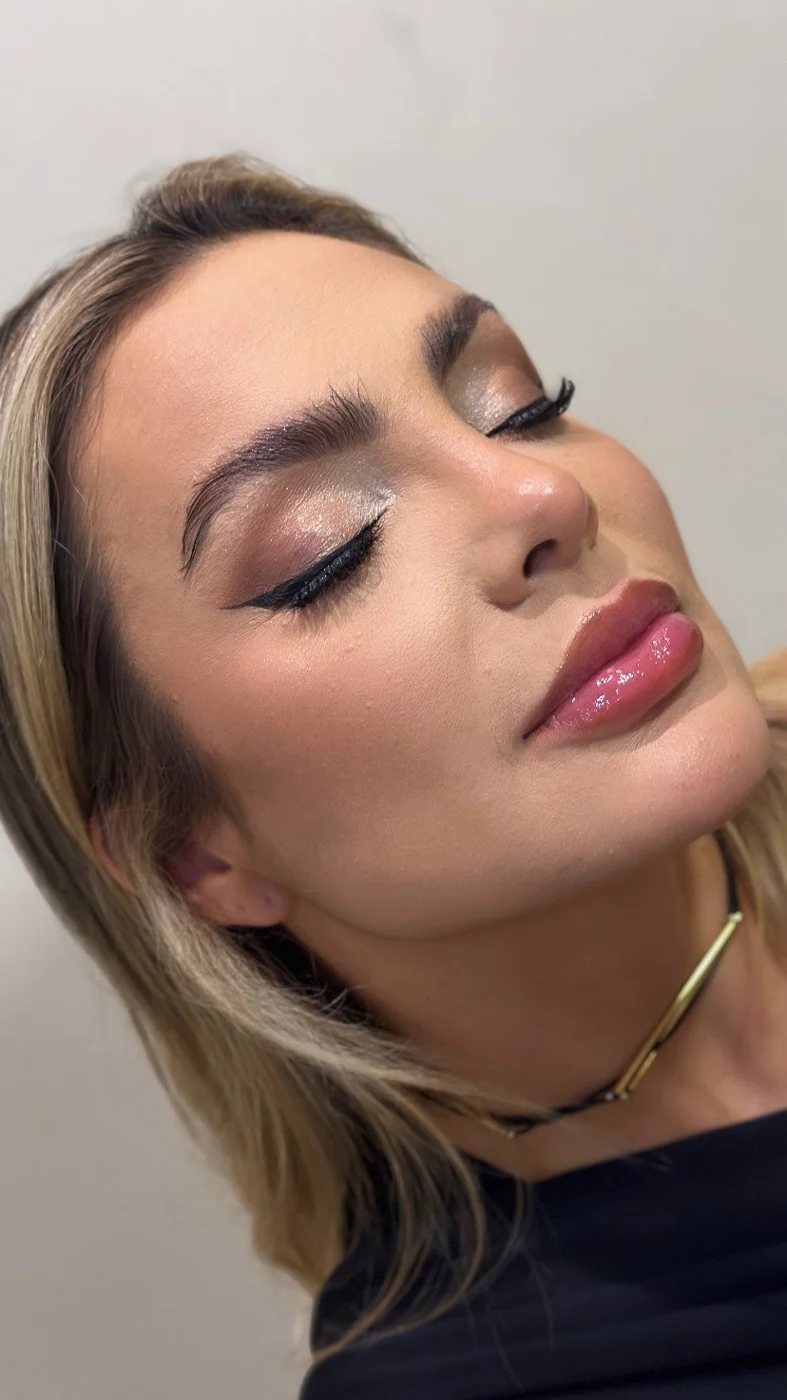 Cliente loira de lado, com delineado, cílios marcados e boca com brilho
