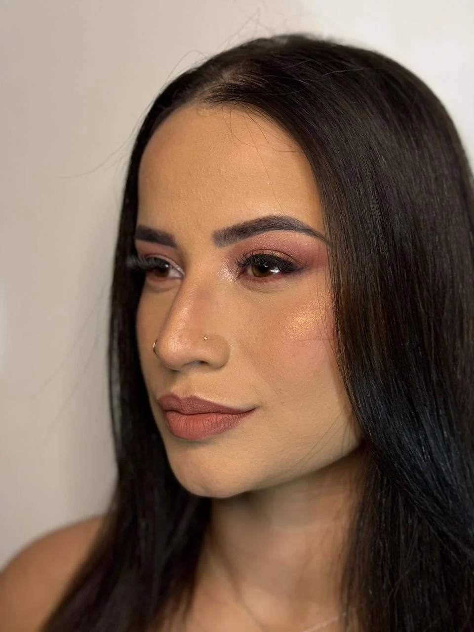 Cliente de cabelo castanho liso, em três quartos, com pele luminosa, sombra rosada e boca nude