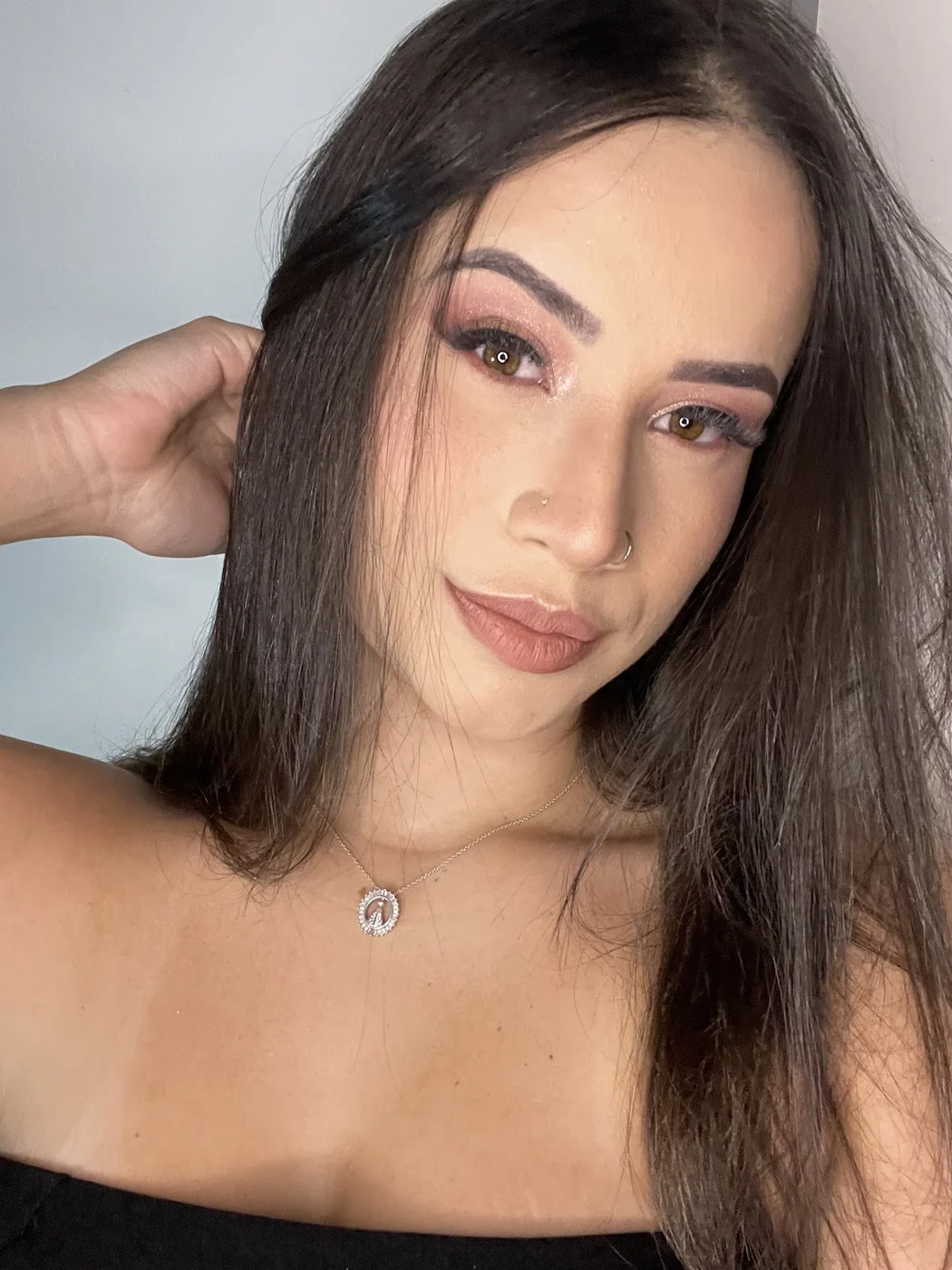 Cliente de cabelo escuro liso com a mão no cabelo, maquiagem suave em tons de rosa